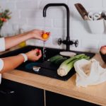 Pessoa lava vegetais em uma pia de cozinha doméstica.