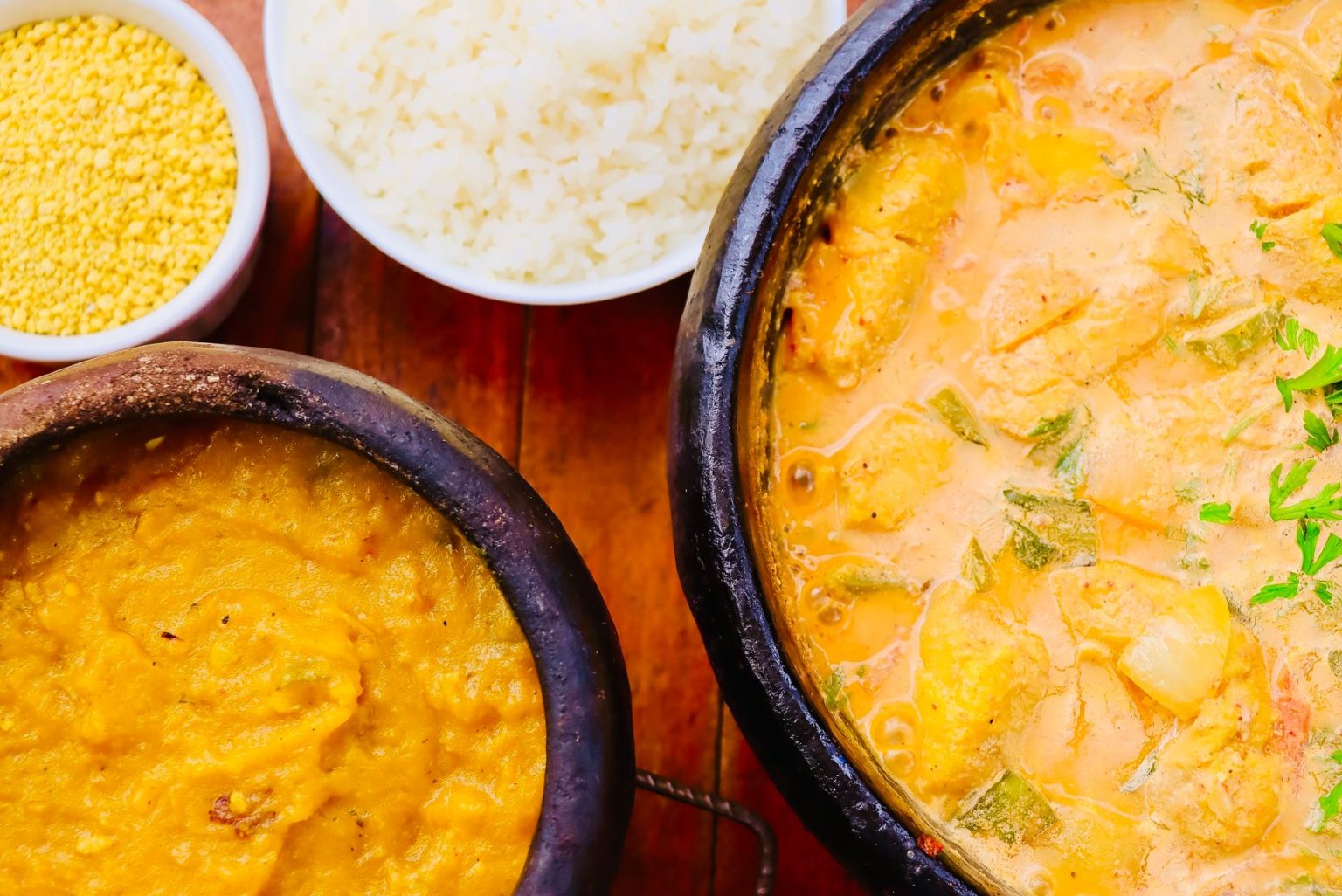 Moqueca brasileira colorida servida em uma panela, acompanhada de outros pratos sobre uma mesa de madeira.