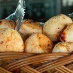 Pães de queijo recém-assados em uma cesta trançada.