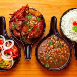 Vista de pratos brasileiros tradicionais com arroz, feijão, carne e salada, servidos em tigelas pretas.