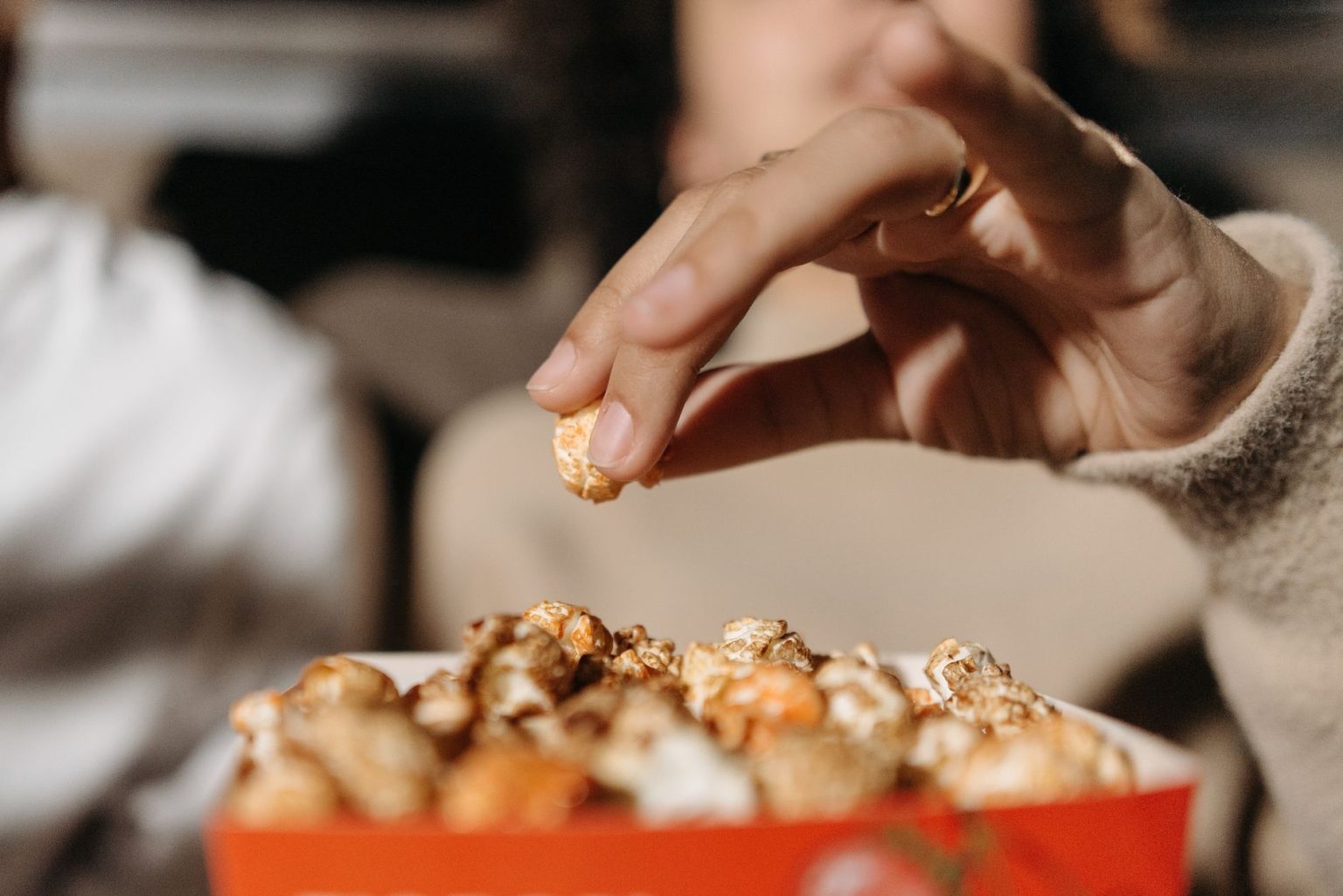 Mão alcança pipoca em uma sala de cinema, ilustrando a relação entre filmes e gastronomia.