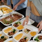 Pessoa prepara marmitas com legumes, feijão e homus para distribuição.
