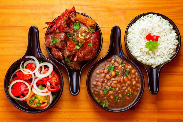 Vista de pratos brasileiros tradicionais com arroz, feijão, carne e salada, servidos em tigelas pretas.